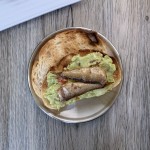 Two Polar brisling sardines on a piece of avocado toast on a small round metal plate.