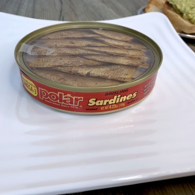 A can of Polar Brisling sardines on a square white plate. The top of the can is a clear plastic film.